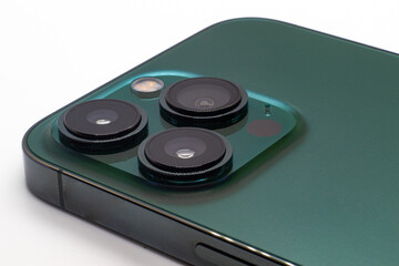 Close-up focused Alpine Green iPhone 13 Pro with 3 big circular cameras, deep green phone backside and cameras isolated on a white surface background with room for diagonal copy space