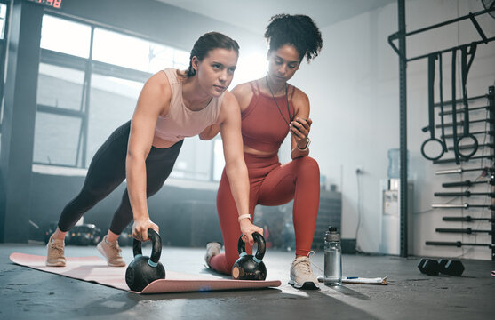 Personal trainer, kettle bell and stopwatch with a black woman coaching a client in a gym for her workout. Health, exercise or training and a female athlete doing a plank with her coach taking time