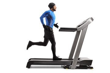 Full length profile shot of a man wearing winter running clothes and exercising on a treadmill © Ljupco Smokovski