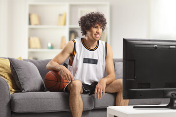 Guy in a sports jersey with a baskteball sitting on a sofa at home