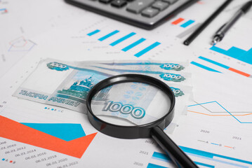 Obraz premium Close-up of money, financial documents with charts, magnifier, pen and pencil at workplace. Low angle view, selective focus of roubles