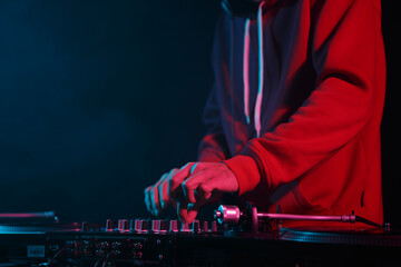 Club dj plays music on stage. Disc jockey in red hoodie playing musical tracks with sound mixer and...
