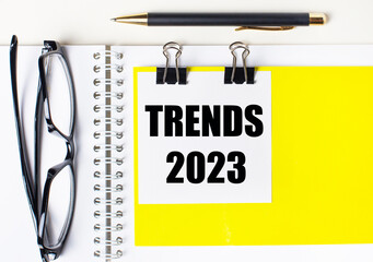 Paper with the text TRENDS 2023 a yellow background, glasses, pen, top view, school, education, knowledge, business.