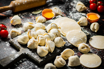 Raw dumplings on a cutting board with egg and flour. 