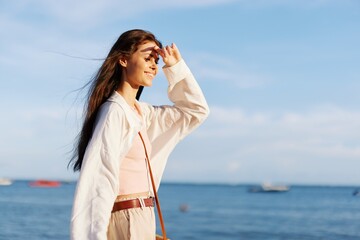 A girl with her eyes closed in the sun against an ocean backdrop smiling with teeth, flying hair, tanned skin, relaxing, traveling to the ocean.