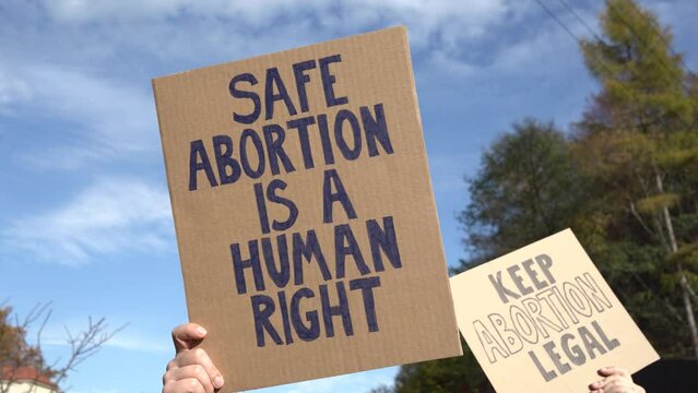 Protesters holding signs with slogans Safe abortion is a human right and Keep abortion legal. People with placards supporting abortion at protest rally demonstration.