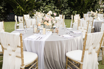 Beautiful outdoor wedding decoration in garden. Round tables decorated with flowers, candles and accessories. Open air wedding banquet on green lawn