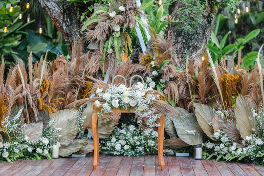 Beautiful outdoor wedding decoration with dry plants, flowers, candles and accessories in garden. Natural, shabby, boho wedding decor. Open air wedding banquet on green lawn
