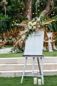 A welcome board sign with a beautiful flower and rustic decoration, standing in front of wedding entrance.