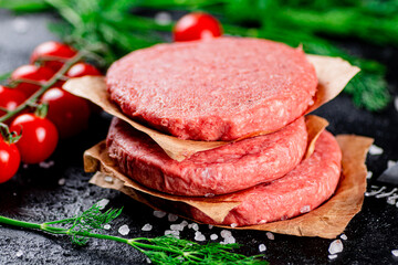 Raw burger on a table with greens and salt. 