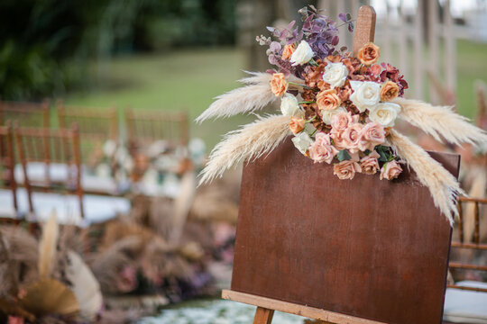 A welcome board sign with a beautiful flower and rustic decoration, standing in front of wedding entrance.