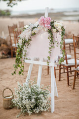 A welcome board sign with a beautiful flower decoration, standing in front of wedding entrance on the beach - 563981915