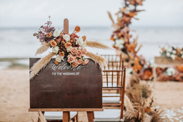 A welcome board sign with a beautiful flower rustic decoration, standing in front of wedding entrance on the beach - 563981974