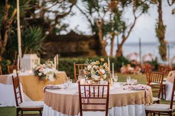 Beautiful outdoor wedding rustic decoration in garden. Round tables decorated with flowers, candles and accessories. Open air wedding banquet on green lawn with sea view