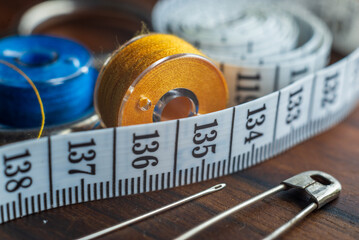 Sewing items - thimble, needle, measuring tape, spools of blue thread, including pins. Blue fabric for sewing on background..