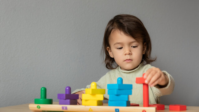 Lifestyle portrait of toddler girl playing with wooden figures, learning shapes and colors