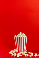 Popcorn in a red and white striped bag on a red background. Front view, copy space