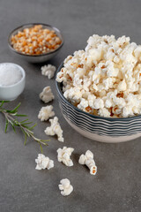 popcorn in a bowl , salt and popcorn kernels on a gray concrete background, close up and selected focus