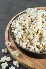 popcorn in a bowl on a wooden board and gray concrete background, closeup and selected focus