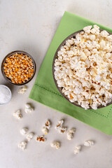 bowl with popcorn, popcorn kernels and salt on a green napkin, on a marble table, top view.