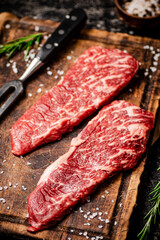 Raw steak with spices on a wooden cutting board. 
