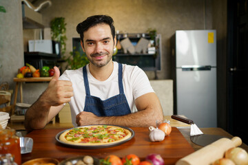 Happy cheerful handsome Italian chef showing a home made baked pizza to camera and smiling.