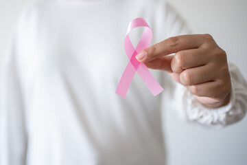 Woman holding pink ribbon as symbol of World Cancer day, breast cancer awareness sign