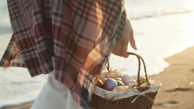 A girl walks along the beach at sunset carrying a basket of Easter eggs. I'm walking towards the sun, the sea waves are behind me.