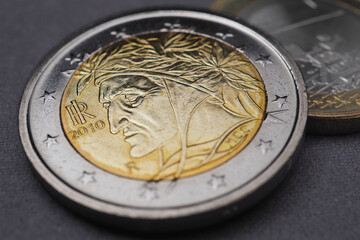 Euro coins closeup. 2 euro coin lies on dark gray surface. Coin issued in Italy. Obverse depicting Dante Alighieri. Dramatic illustration about European Union currency or ECB. EU economy news. Macro