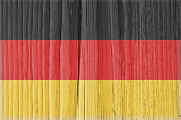 Fototapeta na wymiar Flag of Germany on dry cracked wooden surface. German national symbol. Hard sunlight with shadows on old wood. Vintage background with faded pale vignetting