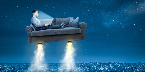 Person with a laptop computer sitting on a flying rocket sofa