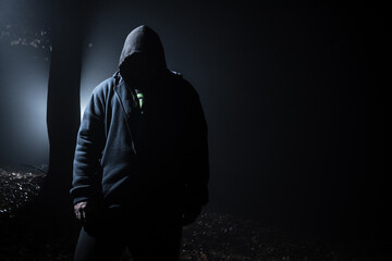 Hooded man in the dark forest at backlight