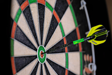 Single black and green dart stuck in the bullseye of a dartboard. Close up of a dartboard.