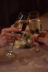 Two glasses with sparkling champagne wine in hands, concept for holiday, bokeh, in a restaurant. Romantic dinner. Man and woman are holding glasses of champagne. Concept for Valentine's day or date