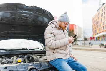 A worried driver is seen holding his mobile phone and standing alone next to his broken down car