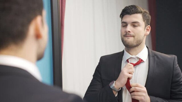 The young man who is late for work prepared in front of the mirror with panic and stress.
Charismatic young man in suit looking at himself in the mirror, being late for work and getting ready in a hur