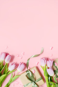  festive layout with tulips, hearts and a gift with green ribbons on a pastel pink background. copy space. top view. flat lay. concept of mother's day, valentines day, eighth of march