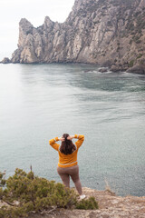 The back view of the plus size woman, a girl with hinged hair admires beautiful nature sea or ocean and rocks