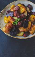 fried colored potatoes appetizing close-up on a clay plate on a dark background