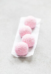 Strawberry mousse cream cake balls sprinkled with coconut chips. On serving paper. Light grey background