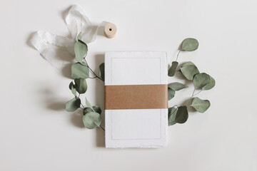 Blank notepad mockup. Cotton paper diary with rough edges, craft belly band, tape isolated on white table background. Dry eucalyptus leaves, branch. Wedding composition, office supply. Flatlay, top. - obrazy, fototapety, plakaty