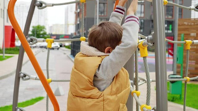 Little boy playing on playground and climbing on the rope ladder. Active child, sports and development, kids playing outdoors.