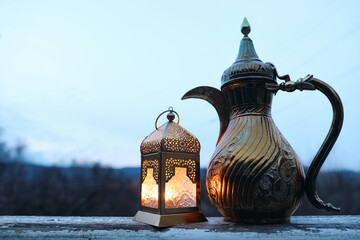 Glowing Moroccan lantern, golden ornamental arabic coffee pot dallah. Outdoor blurred blue evening...