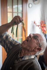 Older man inside a house eating a calçot. Tender onion with typical winter sauce in Catalonia.