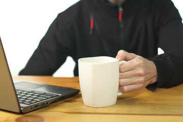person holding a mug with coffee next to a laptop