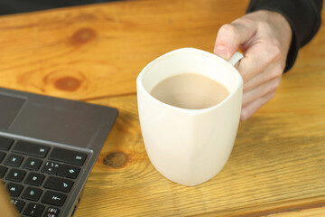person holding a mug with coffee next to a laptop