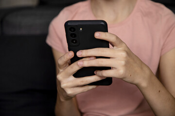 Teenage girl using smartphone, presses her finger, reads social networks on the Internet, types text or makes in-app purchases, mobile phone in two hands.