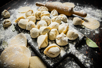 Raw homemade dumplings on a cutting board with a rolling pin. 