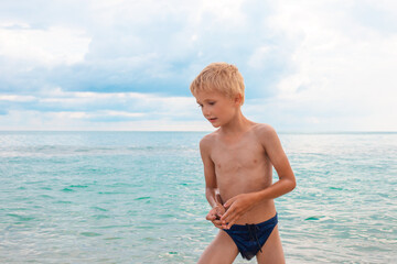 A blond boy in bathing trunks on the beach is resting on summer vacation. A sea adventure © Natalia