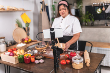 Blurred soft image, an Asian fat woman standing in the kitchen, preparing equipment to make content about pizza homemade. to Influencer Marketing and social media concept.